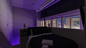 A hotel room with a bed, a nightstand, and a window with a city view. - Downtown Loft Skyline View 2BR (Des Moines)