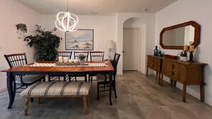 Uma sala de jantar com mesa de madeira, cadeiras, um banco, luminária pendente, planta em vaso, pintura, espelho e um armário.
