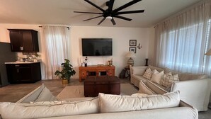 Uma sala de estar com um ventilador de teto, uma TV de tela plana, um sofá, uma mesa de centro, um armário e uma planta.