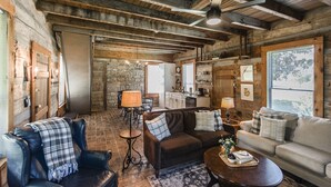 Interior rústico de una cabaña con techo de madera, paredes de piedra y una zona de estar acogedora con sofá y sillones.