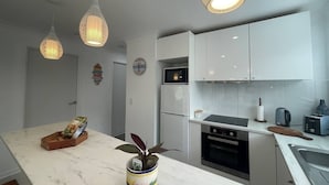 A modern kitchen with white cabinets, a marble countertop, and pendant lighting.
