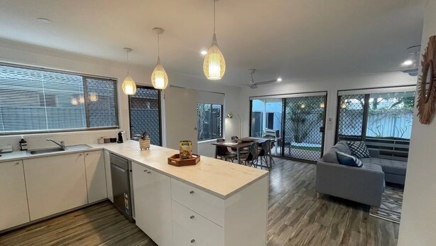 A modern kitchen with a central island, pendant lights, and a dining area with a view of the outdoors.