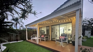 A covered outdoor patio with seating, a wooden deck, and a view of the interior.