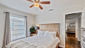 Un dormitorio con cabecera de madera, cama con ropa blanca, ventilador de techo y ventana con persianas.