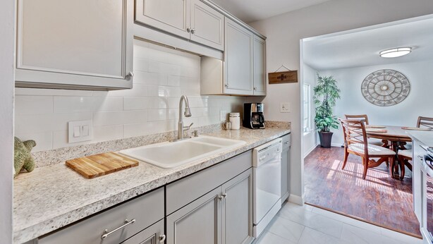 Una cocina moderna con armarios blancos, encimeras de granito, un lavabo doble y una cafetera.