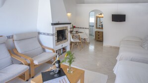 A modern living room with a fireplace, seating area, and a dining table. - Charming Studio with Pool in Praia da Luz (Luz)
