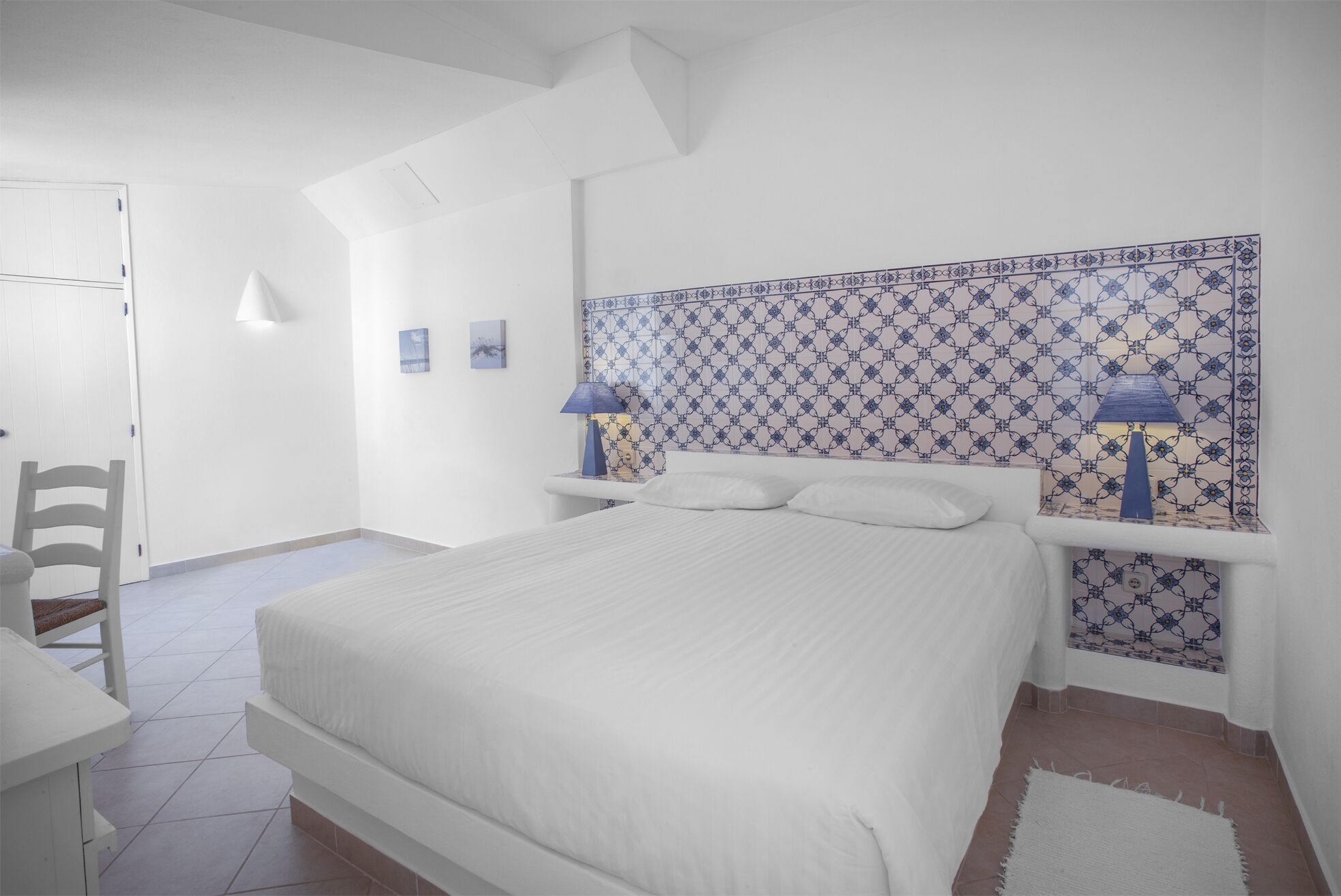 A bedroom with a bed, two bedside tables with lamps, a chair, and a door.