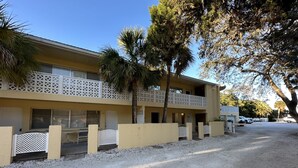 Et toetagers motel med beige facade, hvide gitterbalkoner og palmer i forgrunden.