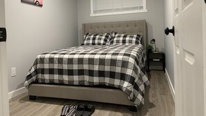 Een slaapkamer met een bed, nachtkastje, raam en deur.