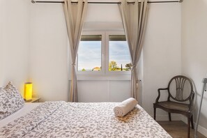 A bedroom with a bed, a chair, a window with curtains, and a lamp.
