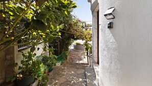 Un estrecho sendero de piedra que conduce a un edificio blanco con una puerta y una lámpara en la pared.