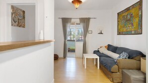 Un salón con sofá, una mesita, suelo de madera y vistas a través de una puerta.