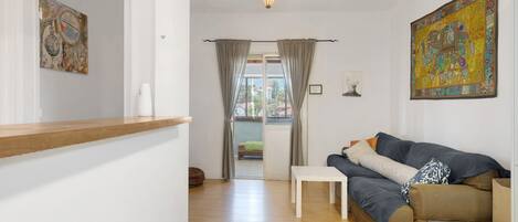 A living room with a sofa, a small table, a wooden floor, and a view through a door.