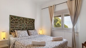 Un dormitorio con cama, lámparas de noche, una ventana con cortinas y una obra de arte en la pared.