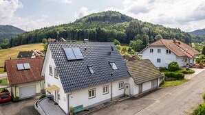 Un quartier résidentiel avec des maisons, une allée pavée et une colline parsemée d’arbres en arrière-plan.