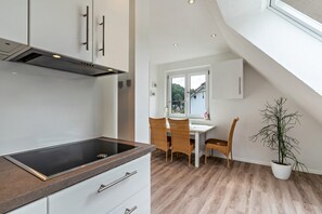 Une cuisine moderne dotée d’une cuisinière intégrée, de meubles blancs et d’un coin repas avec des chaises en osier et une plante en pot.