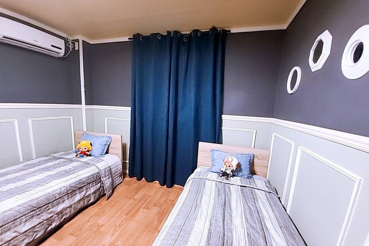 A room with two single beds, a dark curtain, and a wall-mounted air conditioner.