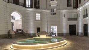 A spacious courtyard with a central fountain, a staircase leading to an upper level, and a large arched doorway. - Nana Inn palazzo nana' (Napoli)