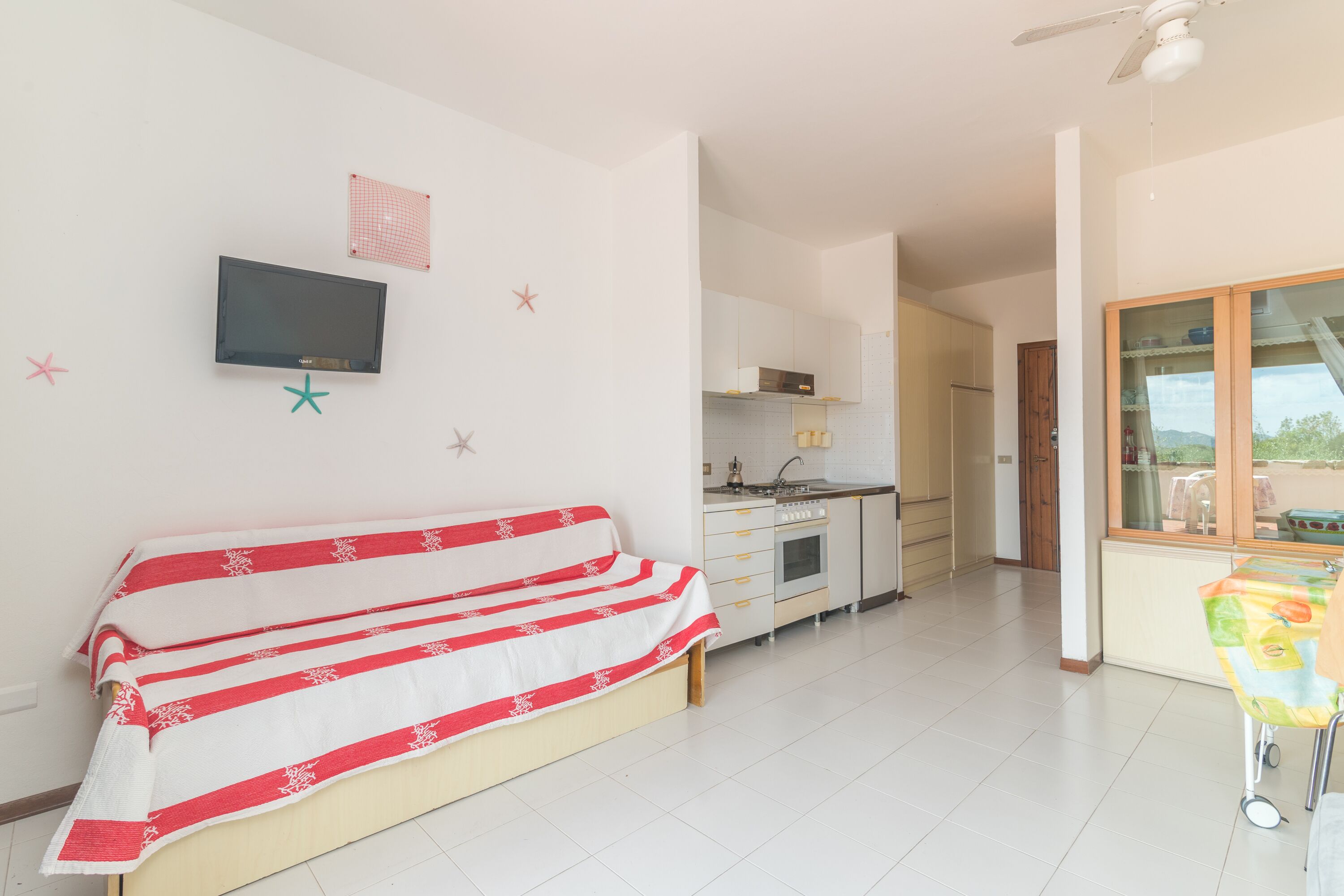 Een kamer met een bed, een televisie aan de muur, een kitchenette en een raam met uitzicht.