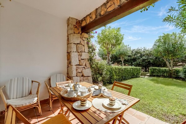 Eine Terrasse mit einem für Tee gedecktem Tisch, umgeben von Korbstühlen, einer Steinmauer und Blick auf einen Garten.