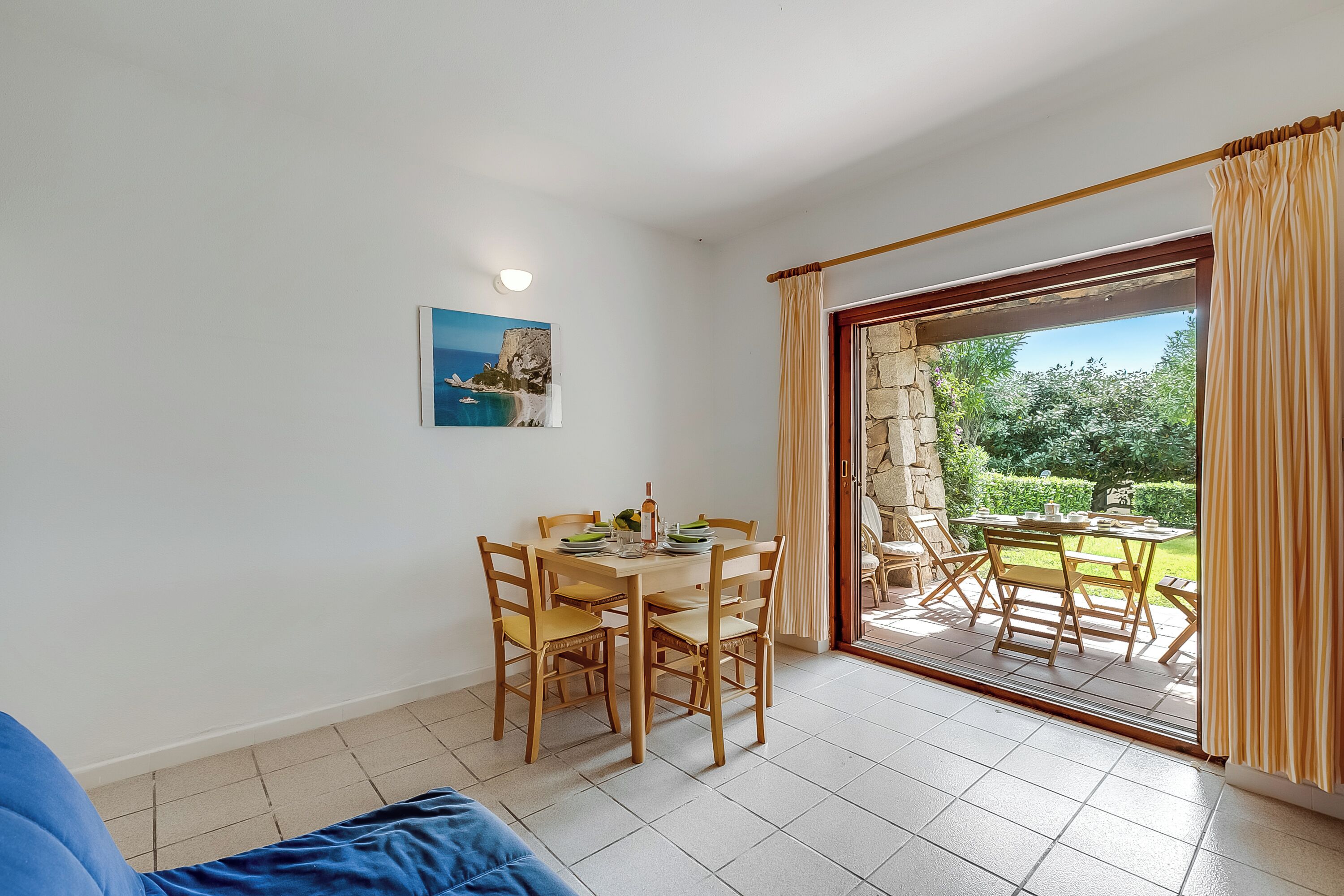 Un comedor con una mesa y sillas, un cuadro en la pared y vista a un patio exterior a través de un ventanal.