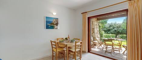 Un comedor con una mesa y sillas, un cuadro en la pared y vista a un patio exterior a través de un ventanal.
