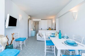 Zona pranzo moderna con tavolo bianco, cuscini blu e TV a parete.