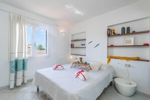 Habitación de hotel con cama, mesita de noche con bandeja, inodoro y ventana con cortinas.