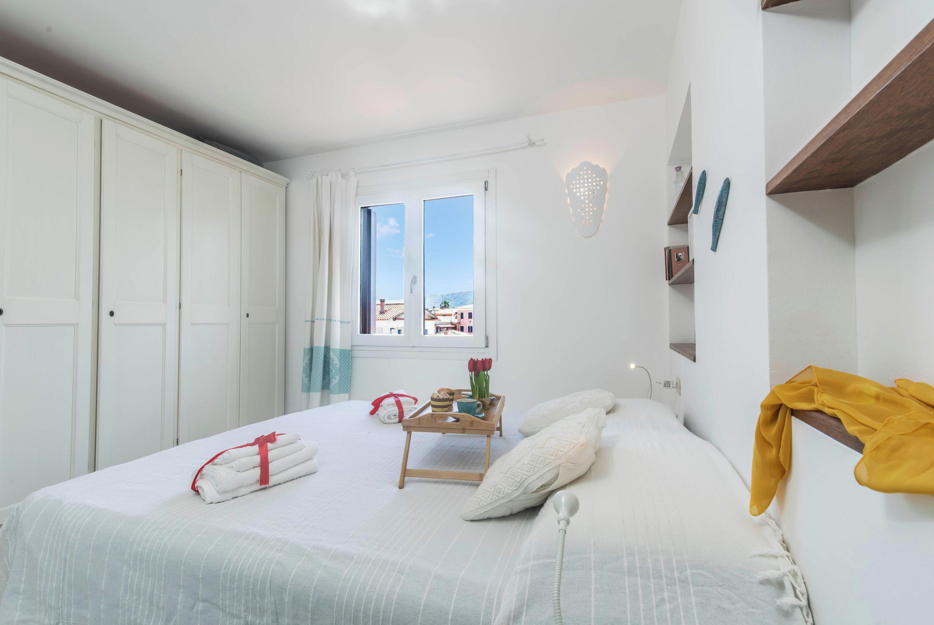 A bedroom with a bed, a window, a bedside table, and a wardrobe.