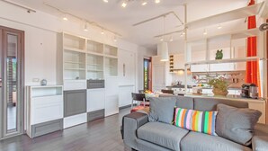 A modern living room with a grey sofa, a colorful striped pillow, and a kitchen area with white cabinets and orange curtains. - Vicerè Apartment With AC and Wi-Fi, Catania, Italy (Catania)