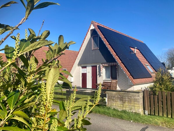 Et hus med et skråt tag, en rød dør og et lille udendørs opholdsområde.