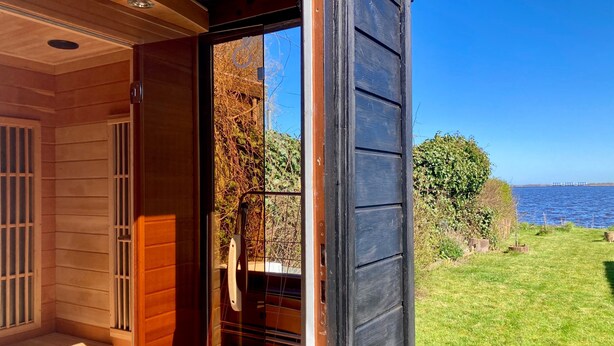 Una cabaña de madera con un cristal que da a un área verde con vista al agua.