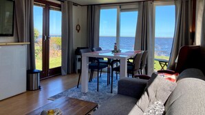 Una sala de estar con una mesa de comedor, sillas, un sofá, un televisor y vista al mar.