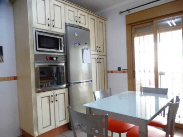 Une cuisine compacte équipée d’un réfrigérateur, d’un four à micro-ondes et d’un four traditionnel. On y trouve une table à manger avec des chaises, ainsi qu’une fenêtre avec des stores.