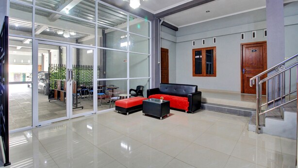 A spacious lobby with a black and red sofa set, a small coffee table, and a staircase. - Hotel O Gm Guest House (Wonogiri)
