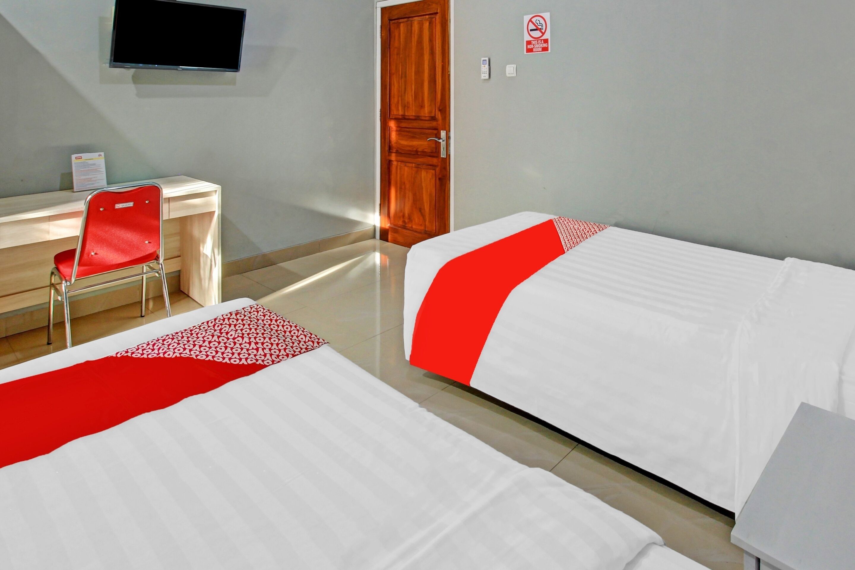 Een hotelkamer met twee bedden, een bureau, een stoel, een televisie en een deur.