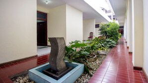 A corridor with a stone sculpture, potted plants, and a tiled floor. - Super OYO 759 Hotel Dewi Sri (Yogyakarta)