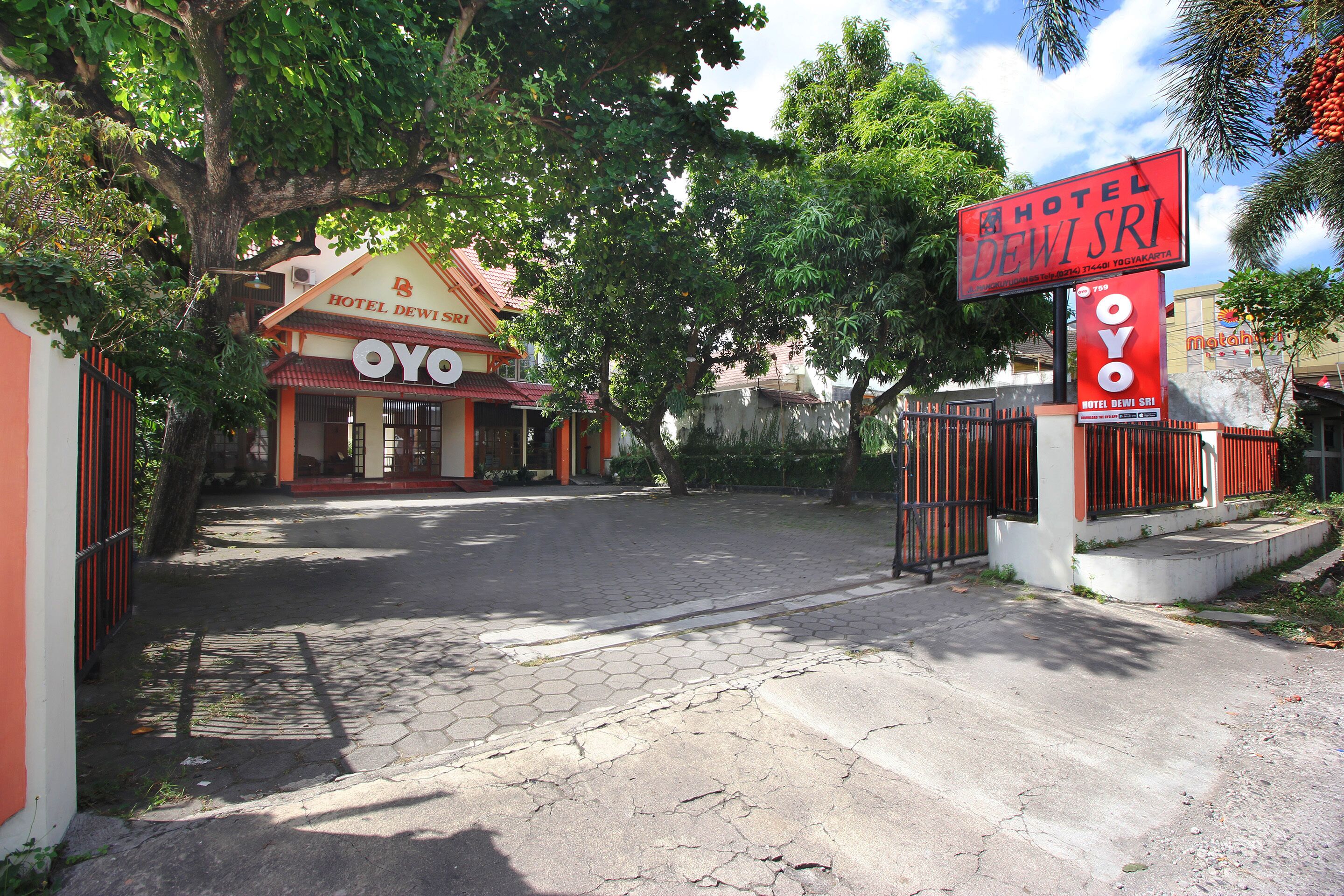 A hotel entrance with a sign for Hotel Dewi Sri and a gated driveway.