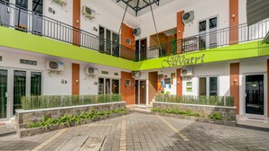 A multi-level building with a green and orange facade, air conditioning units, and a central courtyard with a tiled floor.