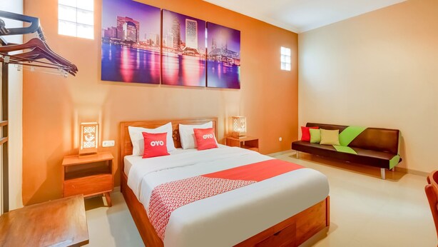 A hotel room with a large bed, a wooden nightstand, a bench, and a wall-mounted TV.