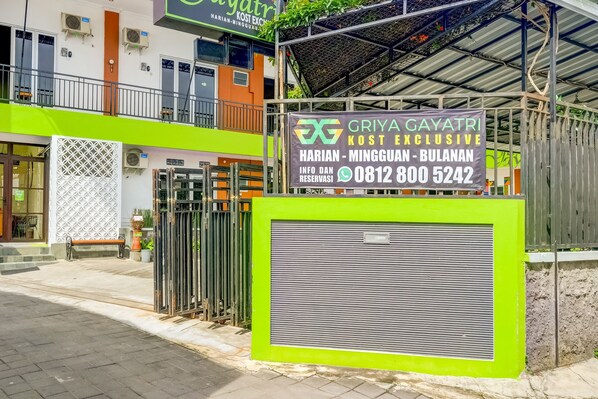 A gated entrance to a building with a sign advertising a hotel named 'Griya Gayatri' and a contact number.