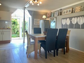 A dining area with a wooden table, dark chairs, a wicker chair, a lamp, and a wall with framed pictures.