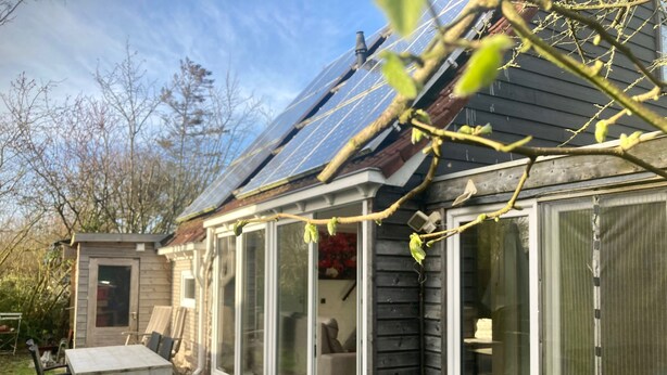 Una casa con porche cubierto, un cobertizo pequeño y un panel solar.