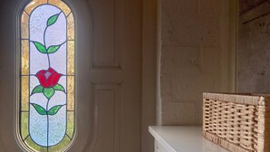 Una habitación con una puerta blanca, un ventanal redondo de vidrio con motivos florales y un armario blanco con una cesta tejida encima.