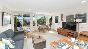 A modern living room with a sofa, coffee table, TV, and dining area with chairs and a table. - Gulf Island View Suite (Chemainus)