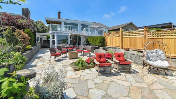 A modern house with a patio area featuring stone flooring, outdoor furniture, and a wooden fence. - Gulf Island View Suite (Chemainus)