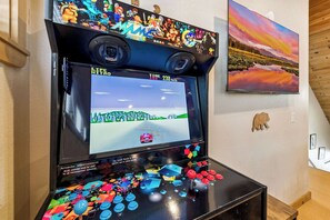 A gaming console with a screen displaying a racing game, a mounted camera, and a painting of a landscape.