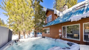 Een bubbelbad in een besneeuwde omgeving, met een houten chalet op de achtergrond.