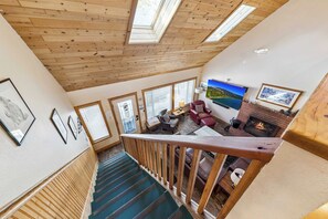 A high-ceilinged room with wooden beams, a fireplace, and a TV mounted on the wall. - 6BR Tahoe Cabin, Hot Tub, Game Room, Near Heavenly (South Lake Tahoe)