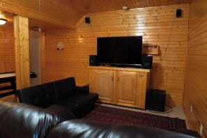 Une pièce aux murs lambrissés, avec un téléviseur fixé sur un meuble, un canapé en cuir noir et un tapis rouge à motifs.